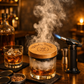 Whiskey- und Cocktail Smoker Set mit drei Holzsorten zur Räucherung, einem Löffel, dem Smoker aus Holz, einem Feuerzeug und einem kleinen Sieb, drapiert auf einem Bar-Tisch
