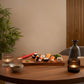 Sushi-Servierbrett aus Holz, mit eingraviertem Fisch, Wellenformen und einer Aussparung für eine kleine Schüssel für die Soja-Soße, platziert auf einem Esstisch mit Kerzen und Flasche